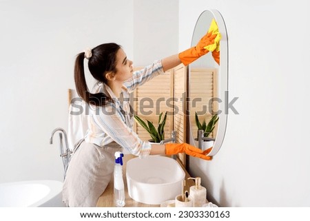 Young woman cleaning mirror in her bathroom Royalty-Free Stock Photo #2303330163