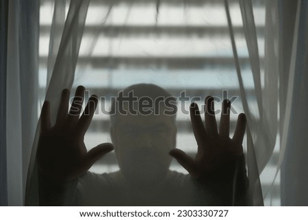 Scary human body silhouette man front of window behind the white  transparent tulle organza curtain. blurred face. 