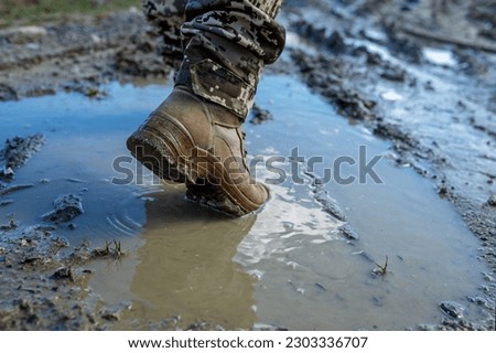 Brown military boots on mud and puddle. Armed Forces of Ukraine. Ukrainian soldier.