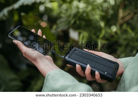Close up of woman charging her smartphone with solar power bank, outdoor in the nature. Royalty-Free Stock Photo #2303340653