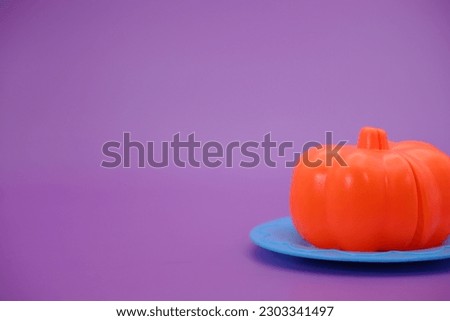 Pumpkin toy that can be split then put back together. toy pumpkin and knife isolated purple background. toy pumpkin on a blue plate.
