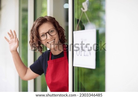 Cafe opening ceremony. Open sign on front door of restaurant or grocery store. Waiter in apron greeting customer. Welcome message on bakery entrance. 