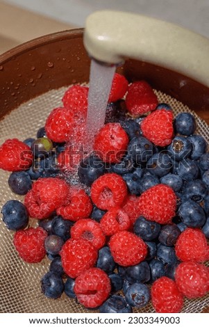 eberries and raspberries washed under cold water tap before eating, lying on a strainer in the sink.
