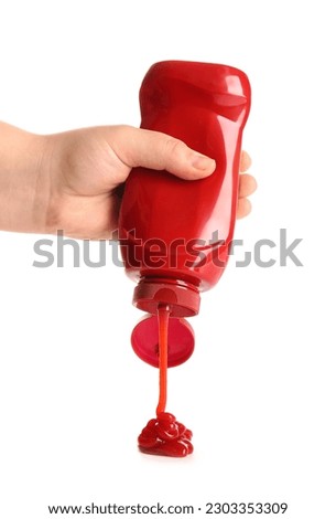 Hand holding ketchup bottle upside down and squeezing on white background Royalty-Free Stock Photo #2303353309