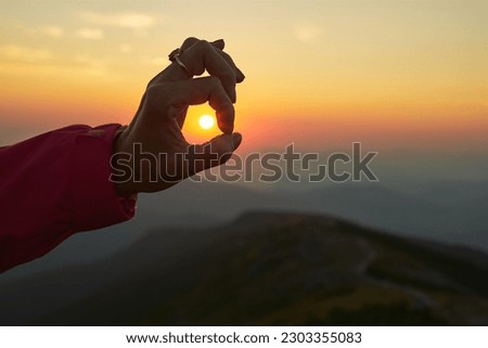 Sun over female hand. Sunrise in mountains. Ready for adventure. Natural mountain landscape with illuminated misty peaks, foggy slopes and valleys, blue sky with orange yellow sunlight