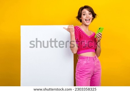 Photo of young funny girl wear pink outfit hold smartphone directing finger poster website ad shopping promo isolated on yellow color background
