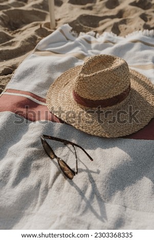 Female sunglasses, straw hat and beach towel on beach sand. Minimal aesthetic lifestyle fashion blog, magazine, social media. Sunbathe, relax, chill on summer travel vacations