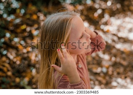 Little girl brushing blonde hair out of her face outside in fall