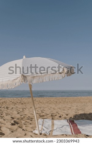 Minimal summer holidays vacation concept. Beach umbrella, beach towel on sand in front of blue sky and sea. Chilling, lounging on the beach