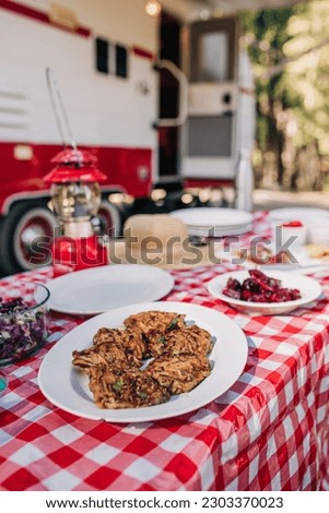 Gourmet Food on a Red and White Tablecloth by an RV with Lantern