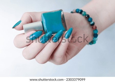 Woman's beautiful hand with long nails and light blue manicure with bottles of nail polish