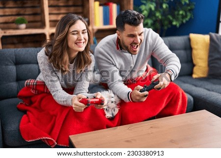 Man and woman playing video game sitting on sofa with dog at home