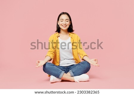 Full body spiritual young woman of Asian ethnicity wear yellow shirt white t-shirt hold spread hands in yoga om aum gesture relax meditate try calm down isolated on plain pastel light pink background