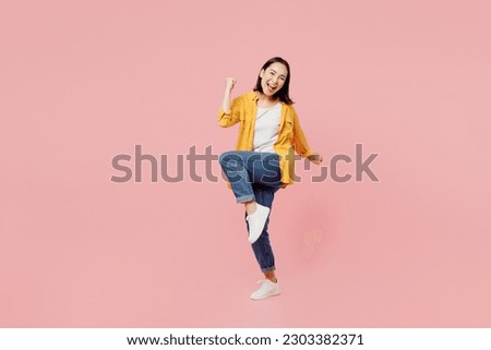 Full body excited young woman of Asian ethnicity wear yellow shirt white t-shirt doing winner gesture celebrate clenching fists say yes isolated on plain pastel light pink background studio portrait Royalty-Free Stock Photo #2303382371