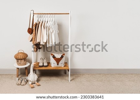 Clothing Rack with kids outfits and storage baskets in children's room. Fashion clothes in white, beige and brown colors on hangers in wardrobe. Set of kids clothes and accessories.   Royalty-Free Stock Photo #2303383641