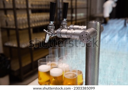 A picture of a cold steamy beer dispenser with glasses of beer in the background.