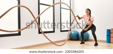 Young beautiful hispanic woman smiling confident using battle rope training at sport center Royalty-Free Stock Photo #2303386205
