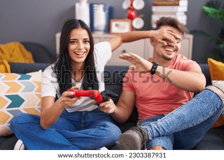 Man and woman couple playing video game sitting on sofa at home