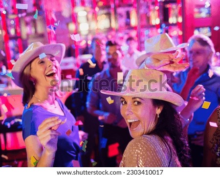 Confetti falling on women wearing cowboy hats laughing dancing in nightclub