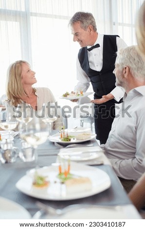 Waiter serving fancy dish to woman sitting at restaurant table Royalty-Free Stock Photo #2303410187