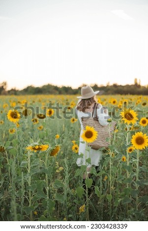 Portrait of beautiful young woman 33 years old in hat in sunflower field at sunset. Happy model in white dress on summer evening in nature.