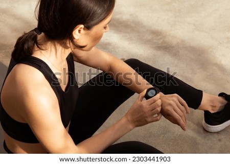 Tired millennial european woman athlete in sportswear checks pulse on fitness tracker in city, outdoor. Result body care, cardio training and fitness, gadget for active workout Royalty-Free Stock Photo #2303441903