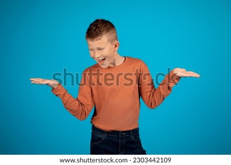Cheerful caucasian boy making scales with his palms and comparing options, happy preteen male child holding invisible objects in hands, making choice while posing over blue background, copy space