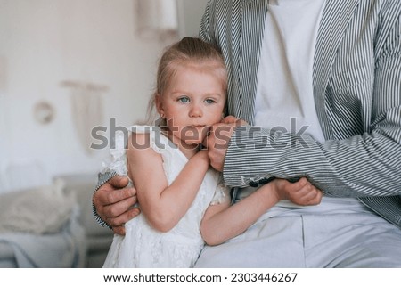 Cropped shoot of father calming little blonde daughter frustrated, needs more attention. Upset little girl in white dress holding fathers hand at home. Affection, fatherhood. Confused preschooler. Royalty-Free Stock Photo #2303446267