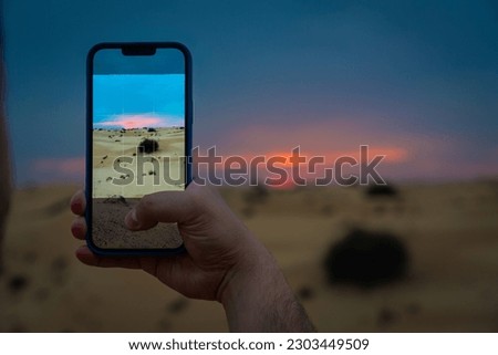 A young man takes a picture with his mobile phone of the desert outside Dubai at sunset.