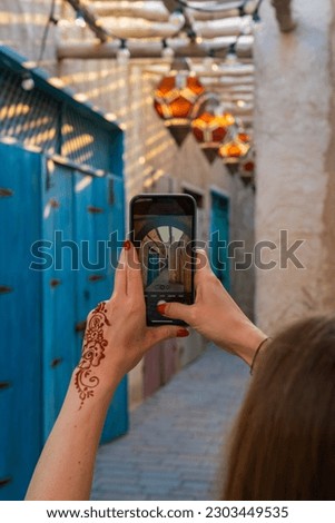 A young woman with henna on her hand takes a picture with her mobile phone in a deserted alley in Dubai Market.