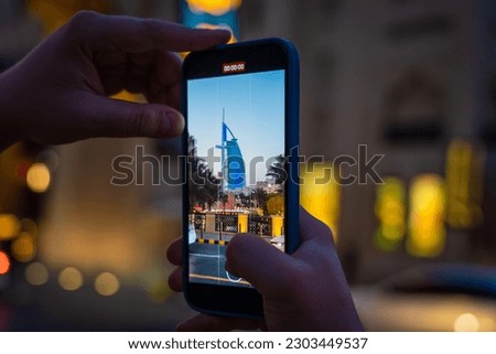 A young woman takes a mobile phone video of Dubai's Burj Al Arab hotel during the blue hour after sunset.