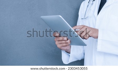 Digital solution for medical science. Smiling young doctor in white uniform working on digital tablet while standing against grey background