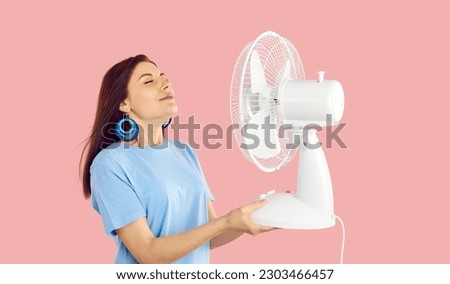 Overheated millennial girl isolated on pink studio background hold fan breathe fresh air. Unwell thirsty young woman use ventilator suffer from hot summer weather. Heatstroke and ventilation. Royalty-Free Stock Photo #2303466457