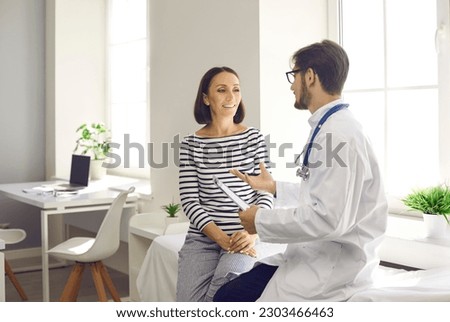 Happy middle-aged female patient talking to her family doctor in hospital office. Woman listens to advice of doctor sitting on couch by window. Concept of medical advice. Royalty-Free Stock Photo #2303466463