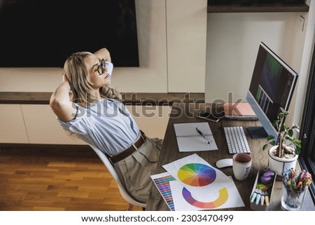 Young female freelancer designer sitting with her hands behind her head and relaxing while working in her home studio.