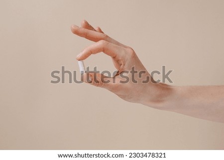 Female hand holding white pill with fingers on beige isolated background. Concept of health care, dietary supplements, treatment of depression and diseases Royalty-Free Stock Photo #2303478321