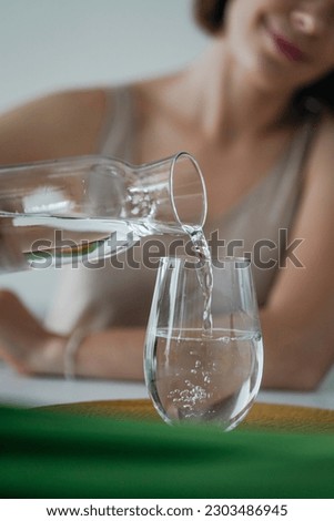 Young woman is pouring purified fresh drink water from bottle into the glass close up. Texture of  the clean water. Healthy lifestyle. Drinking importance Royalty-Free Stock Photo #2303486945