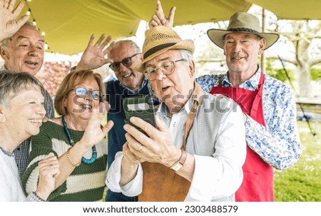 A group of retired friends enjoys using technology during an outdoor barbecue. The seniors enjoy using technology, taking selfies and making video calls.