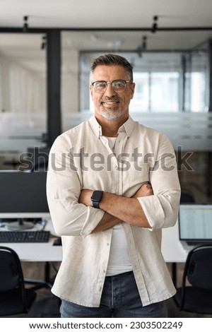 Handsome hispanic senior business man with crossed arms smiling at camera. Indian or latin confident mature good looking middle age leader male businessman on blur office background with copy space.  Royalty-Free Stock Photo #2303502249