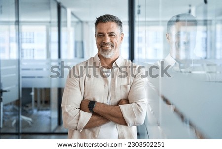Handsome hispanic senior business man with crossed arms smiling at camera. Indian or latin confident mature good looking middle age leader male businessman on blur office background with copy space.  Royalty-Free Stock Photo #2303502251