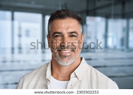 Headshot close up portrait of indian or latin confident mature good looking middle age leader, ceo male businessman on blur office background. Handsome hispanic senior business man smiling at camera. Royalty-Free Stock Photo #2303502253