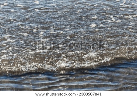 Close-up image of gentle waves rippling as they reach the seashore on a sandy beach.