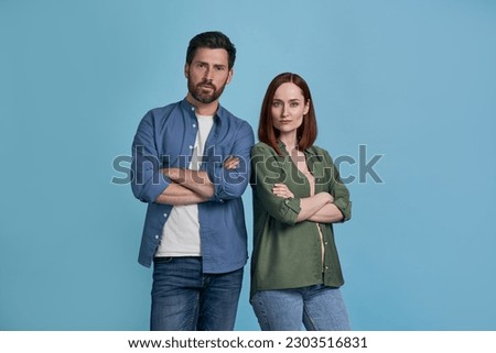 Portrait of serious handsome man and confident red haired woman holding arms crossed looking at camera isolated on blue background. Successful business 