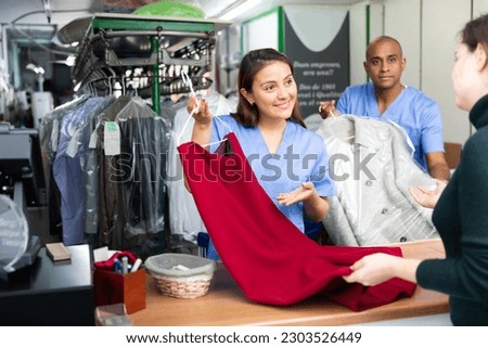 Ordinary woman and man working with client in modern laundry, receiving clothing for dry cleaning Royalty-Free Stock Photo #2303526449