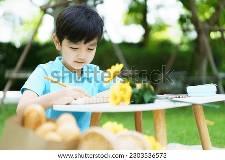 Happy cheerful Asian little boy enjoy drawing and painting alone at home backyard alone, boy drawing a picture at outdoor garden portrait on a beautiful natural bokeh background.
