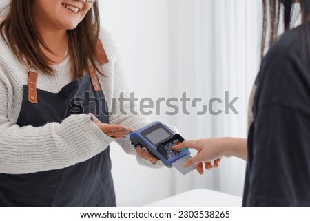 Photo of smiling asian girl barista, giving client POS terminal, help pay with credit card, standing at counter in coffee shop, working in cafe.