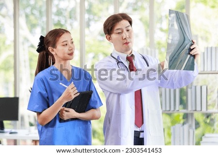 Asian handsome professional successful male doctor in white lab coat with stethoscope holding xray film talking brainstorming with female assistant nurse in blue uniform in clinic hospital office.