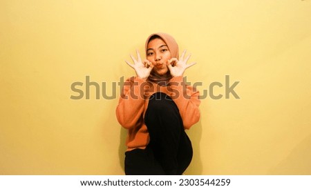 Attractive beautiful Asian woman sitting on chair with happy feeling of happiness isolated on orange background.