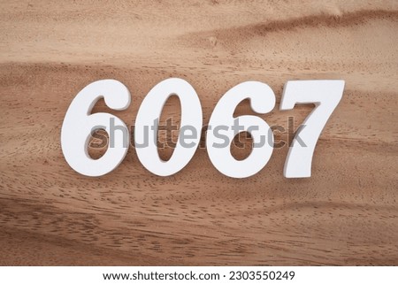 White number 6067 on a brown and light brown wooden background.
