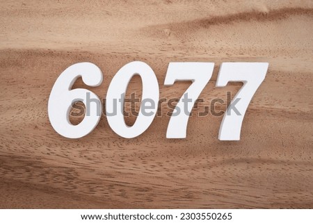 White number 6077 on a brown and light brown wooden background.